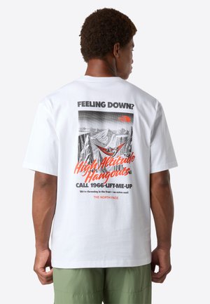 Man in green shorts wearing white T-shirt with mountain graphic and text: "Feeling down? High Altitude Hangouts Call 1966-LIFT-ME-UP."