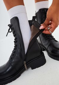 Botas de tobillo de cuero negro con una superficie texturizada, un cierre lateral con cremallera y una suela gruesa negra. En el interior, se aprecia un suave forro marrón.