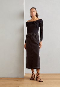 Svart off-shoulder bodysuit med r gathered detaljer, parat med en högmidjad mörk denimkjol med fransat nederkant och svarta remsandaler.