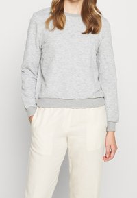 Sudadera gris con textura, cuello redondo y puños acanalados, combinada con pantalones de color claro. Tela suave con un patrón uniforme.