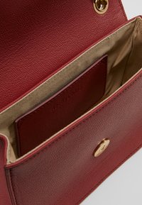 Röd läderhandväska med texturerad yta, med en beige innerfoder och en snap-stängning i guldfärg. Inkluderar en kortfack.