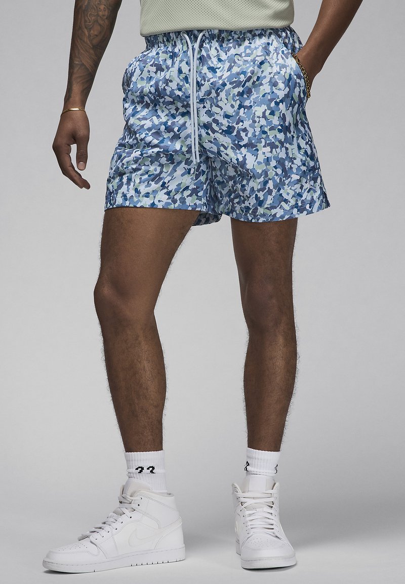 Shorts de bain camouflage bleus avec une taille élastique, cordon de serrage blanc et poches latérales. Associés à des baskets montantes blanches.