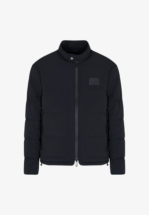 Veste matelassée noire pour homme avec col montant, fermeture éclair frontale, poches latérales et petite écusson rectangulaire sur la poitrine.