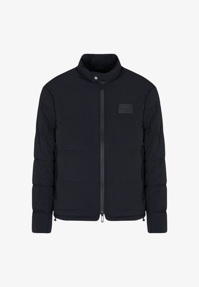 Veste matelassée noire pour homme avec col montant, fermeture éclair frontale, poches latérales et petite écusson rectangulaire sur la poitrine.