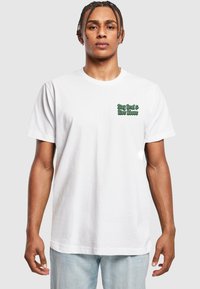 T-shirt en coton blanc à manches courtes, avec un texte vert "Reste vrai & Élévation" sur la poitrine gauche. Ourlet droit et coupe décontractée.