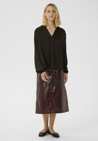 Zwarte V-hals blouse met lange mouwen, gecombineerd met een bordeauxrode, glanzende rok tot halverwege met een gladde textuur en afscheidingdetails.