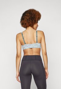Sutiã desportivo com padrão azul claro e alças ajustáveis em teal. Usado com leggings pretas de cintura alta com detalhes de costura contrastantes.