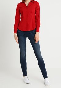 Röd långärmad skjorta med knappar, figursydd design, kombinerad med mörkblå tighta jeans och vita sneakers, enkla rena linjer, inga synliga mönster.