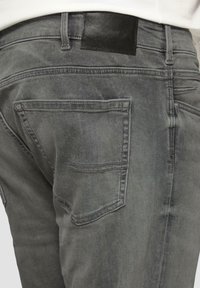 Szare dżinsy z denimu z skórzaną łatą w talii oraz dwoma tylnymi kieszeniami z subtelnymi detalami szycia. Gładka tekstura.