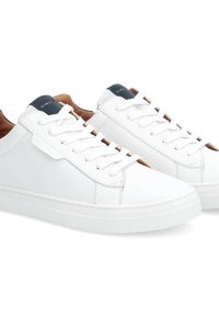 Baskets blanches en cuir avec une semelle en caoutchouc texturé, des lacets plats et une doublure intérieure contrastante en marine. Design simple avec des accents minimalistes.