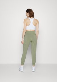 Calças de jogging verdes com um design afunilado, cintura elástica e punhos canelados, combinadas com um top cropped branco de alças para as costas.