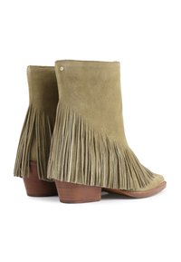 Bottes de cheville en suède vert olive avec des franges sur les côtés et un talon en bois brun empilé. Aucun matériel ou embellissement visible.