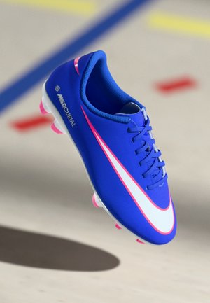 Modré kopačky Nike Mercurial na futbal s bielym a ružovým logom, ružovými čapmi a šnúrkami na rozmazanom vnútornom ihrisku.