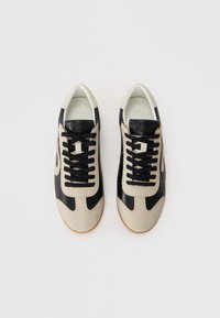 Sneaker basse nere e beige con tomaia in pelle, lacci neri piatti, suola in gomma e marchio sulla linguetta. Texture liscia e design a contrasto.