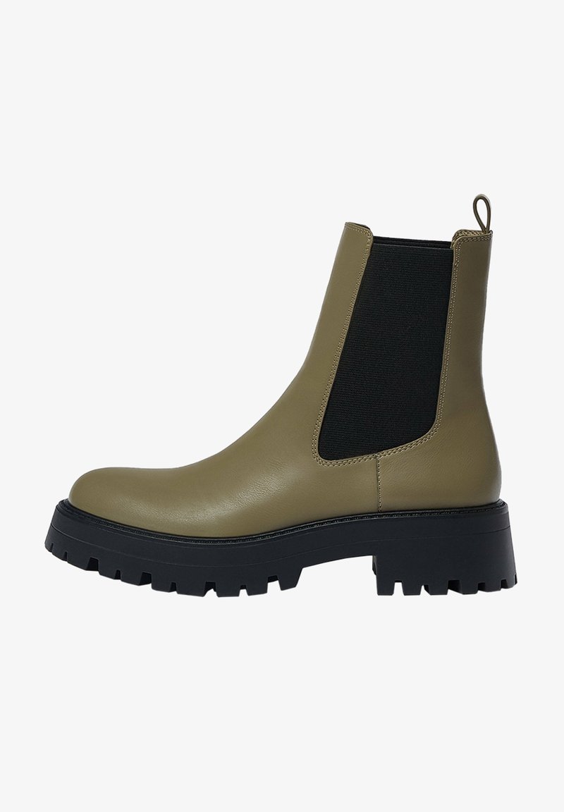 Botte Chelsea en cuir vert olive avec une semelle épaisse noire à crampons, un panneau latéral élastique et une languette à l'arrière.