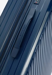 Navy blue hard-shell suitcase with vertical grooves, a textured surface, a molded handle, and a combination lock for security.