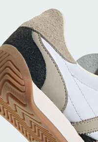 Scarpa sportiva realizzata con materiali a strati: suede beige, tessuto nero testurizzato e pelle bianca. Suola in gomma con un motivo a zigzag.