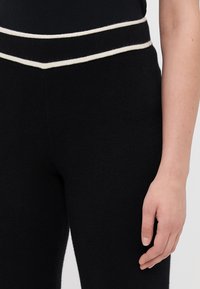 Pantaloni negri dintr-un material texturat, cu un design ajustat, având o dunga crem contrastantă pe talie.