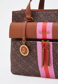 Brun mønsteret tote bag med en glat brun klap, guldfarvet hardware og pink og røde striber. Har en aftagelig logocharms og tekstureret finish.