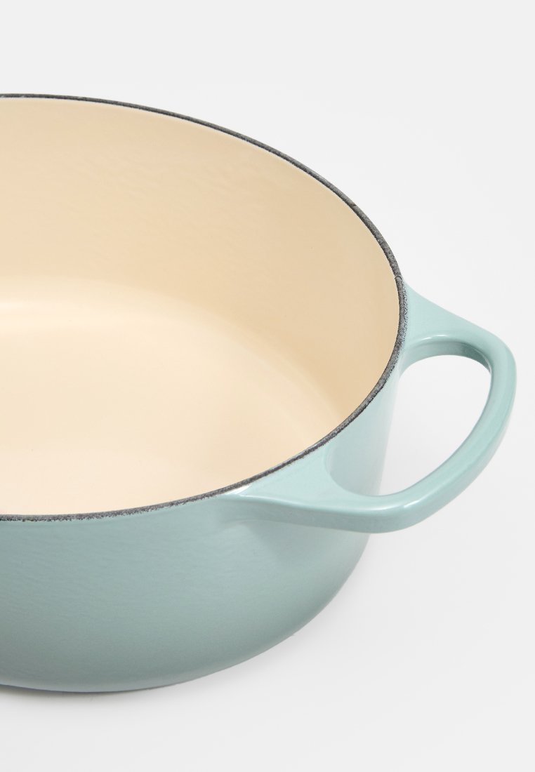 Gieten pot met een lichtblauwe buitenkant en een beige binnenkant. Heeft twee handgrepen, een gladde textuur en een lichte glans. Geen deksel.