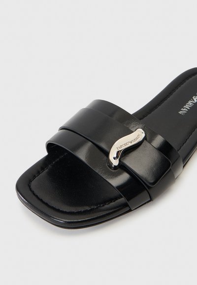 Sandale mule en cuir noir à bout ouvert avec deux larges brides et une boucle argentée incurvée gravée "EMPORIO ARMANI" sur un fond uni.