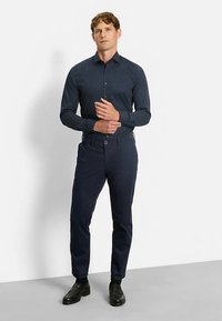 Chemise bleu foncé à boutons avec un petit motif à pois blancs, associée à un pantalon slim bleu marine foncé et des chaussures habillées noires.