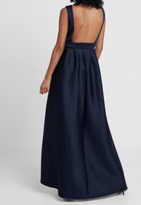 Abito blu navy con un corpetto aderente e una schiena scoperta. Presenta spalline sottili e una gonna fluida che si estende fino al pavimento. Tessuto liscio.