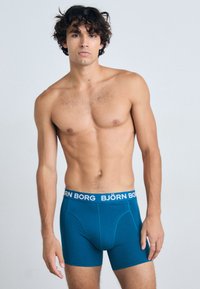 Boxers em teal com uma cintura branca "BJÖRN BORG", textura suave, ajuste justo e sem padrões visíveis ou acentos adicionais.