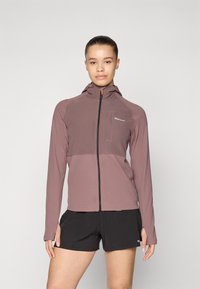 Veste légère à capuche en mauve avec fermeture éclair sur le devant, panneau contrastant et poche poitrine. Comprend des manches longues et des trous pour les pouces.