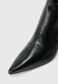 Sorte lær ankelsko med spiss tå, glatt tekstur og detaljert søm. Skaftet har et slankt design med minimalt preg.