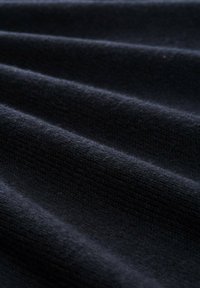 Tessuto di un blu navy scuro con una superficie morbida e texture, caratterizzato da sottili righe verticali e una leggera lucentezza, disposte in delicate pieghe.
