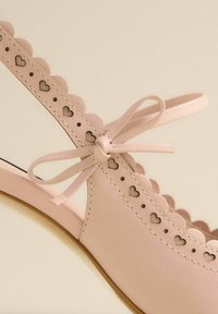 Scarpa slingback in pelle rosa con bordo scallopato, intagli a forma di cuore e dettaglio a fiocco. Texture liscia con cuciture a contrasto.