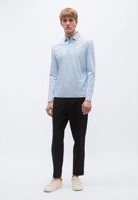 Φωτεινό γαλάζιο πόλο με μακριά μανίκια και γιακά, συνδυασμένο με μαύρο παντελόνι με στενή εφαρμογή και μπεζ αθλητικά παπούτσια, διαθέτει απλό σχέδιο και λείο ύφασμα.