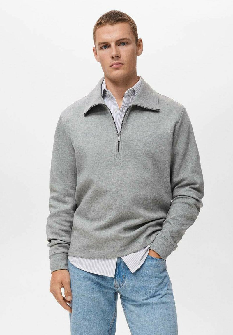 Grijze zip-up sweatshirt met een hoge kraag, met lange mouwen en een ontspannen pasvorm, gedragen over een lichtgestreept shirt en blauwe jeans.