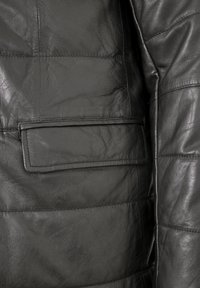 Schwarze Lederjacke mit einer gesteppten Textur, einer einfachen rechteckigen Tasche und sauberem Nähen. Das Material wirkt weich und leicht glänzend.