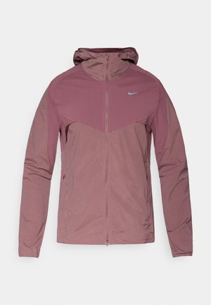 Ελαφρύ μπουφάν Nike σε απαλή μωβ απόχρωση, με φερμουάρ μπροστά, κουκούλα και μπλε λογότυπα. Υφασμα με υφή και αθλητικό σχέδιο.