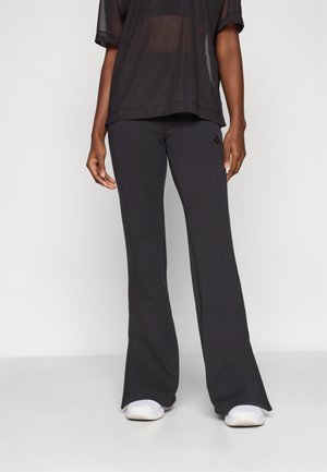 Top transparent negru și pantaloni evazați gri închis cu un logo Adidas pe lateral. Ținuta are o croială lejeră și o textură a țesăturii netedă.