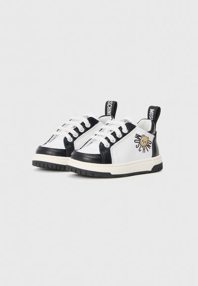 Svarte og hvite barnesneakers med en glatt skinnoverdel, rund tå, hvite snørebånd og en bjørnlogo som akcent på siden.