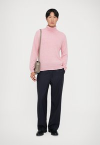 Roze gebreid coltrui gecombineerd met marineblauwe gestreepte broek met wijde pijpen. Het model houdt een kleine grijze schoudertas vast.