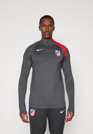 Nike langærmet træningstop i mørkegrå, med en rød skulderdetalje og Atlético Madrid-logo på brystet. Glat, atletisk pasform.