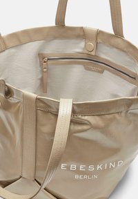 Borsa a tracolla beige con materiale liscio e lucido. Presenta due manici robusti, una tasca interna con zip e il nome del marchio stampato in bianco.