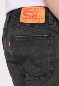 Primer plano de unos jeans de mezclilla negros que muestran la etiqueta naranja de Levi Strauss en la cintura y una pequeña etiqueta roja en el bolsillo trasero.