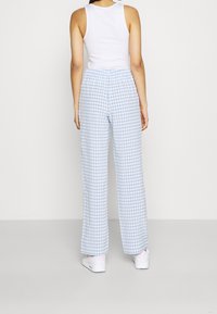 Ljusblå rutiga vida byxor i gingham med en slät tygtextur, bärs med en vit linne och vita träningsskor.