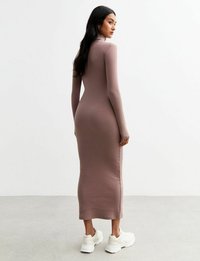 Robe ajustée à manches longues en tissu mauve, présentant un col montant et une silhouette droite, associée à des chaussures de sport blanches.