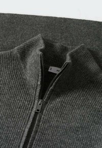 Grauer Strickpullover mit hohem Kragen und einem Frontreißverschluss. Merkmale eine gerippte Textur und einen subtilen Glanz. Die Metallreißverschlussbeschläge sind sichtbar.