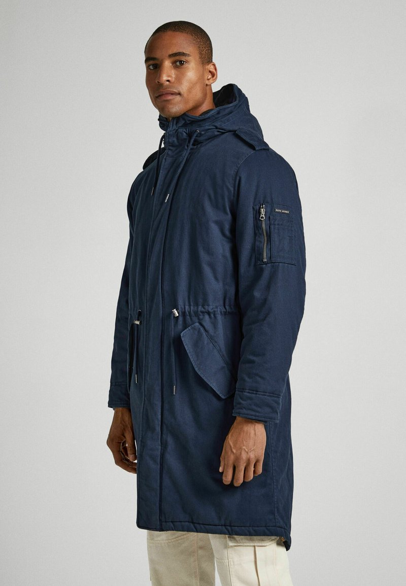 Giacca parka navy con cappuccio, vita regolabile con cordino elastico, tasca a zip sul petto e grandi tasche laterali, finitura in tessuto liscio.