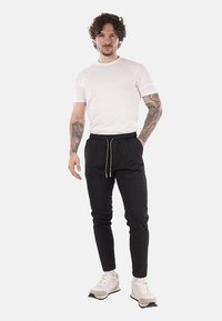 Pantalones de chándal negros con una cintura elástica y cordón, combinados con una camiseta blanca y zapatillas ligeras. Presenta un diseño ajustado.