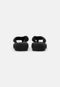 Sandales noires avec une sangle tissée texturée, semelle plate et support de voûte plantaire rembourré. Design minimaliste sans aucune marque ou logo visible.