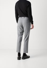 Grey tailored trousers with a slim fit, featuring back pockets, smooth texture, and a cuffed hem. Worn with a black long-sleeve top.
