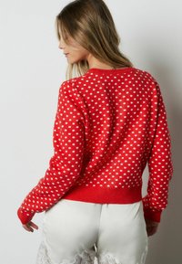 Punainen villapaita, jossa on valkoinen pilkkukuosi. Mallissa on resorireunainen kaulus ja hihansuut sekä hieman väljä istuvuus.